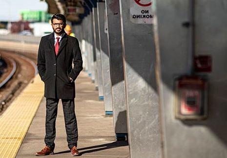 一个穿西装的男人双手插在口袋里站在高架火车站台上.